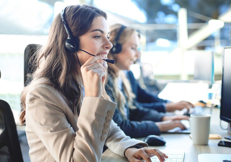 Photo female customer support operator with headset and smiling, with collegues at background.