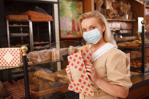 Female customer wering medical face mask, buying bread at the bakery during coronavirus pandemic