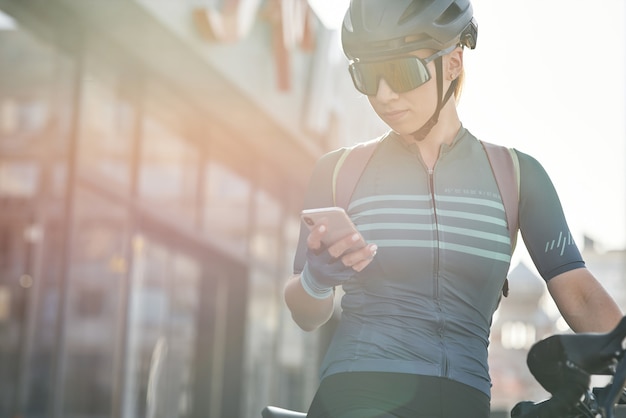 市内中心部のスポーツウーマンで自転車に乗っている間スマートフォンを使用して保護具の女性サイクリスト