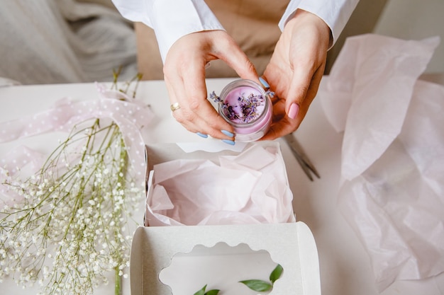 female decorator puts a decorative pink candle in a white gift box nearby are flowers