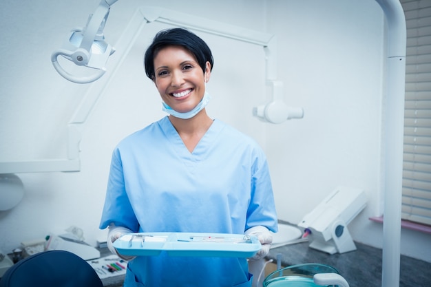 Female dentist in blue scrubs holding tray of tools