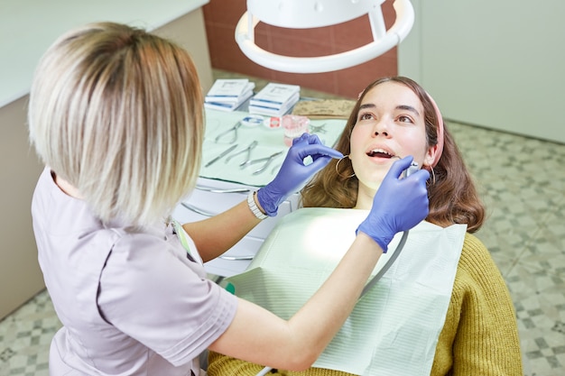 Female dentist checking patient girl teeth at the dental clinic office. Stomatology and health care concept.