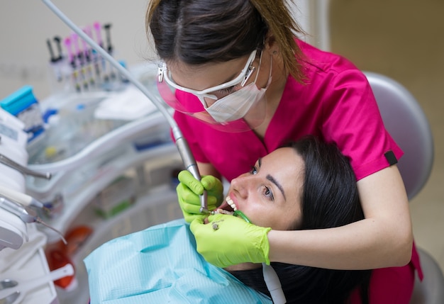 치과 병원에서 아름다운 환자 여성의 치아를 청소하는 여성 치과 의사