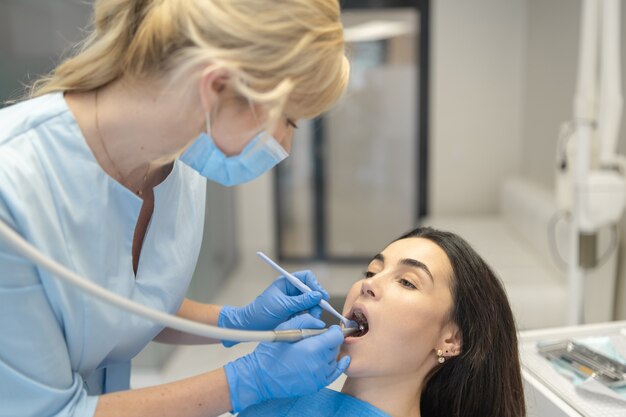 Female dentist in dental clinic providing examination and treatment of oral cavity for female patient