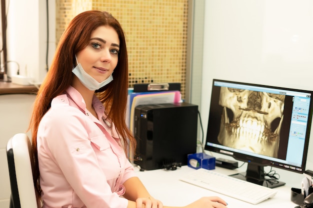 A female dentist doctor is sitting at a table, on a computer