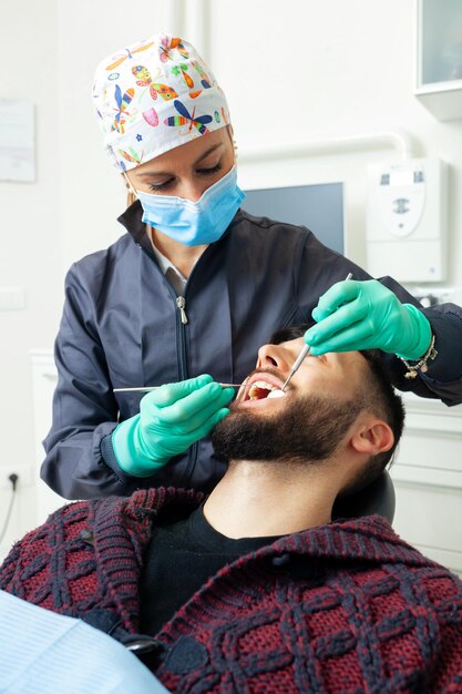 Female dentist examines a man patient in a dental office using professional tools