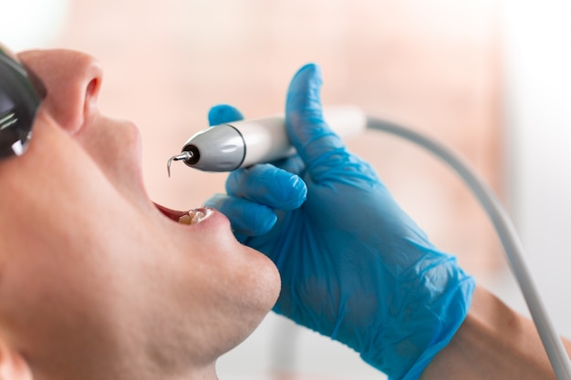 A female dentist examines the oral cavity of the patient with a tool with a mirror. Close-up portrait of a patient with a mouth open, a doctor in gloves holds a dental mirror.