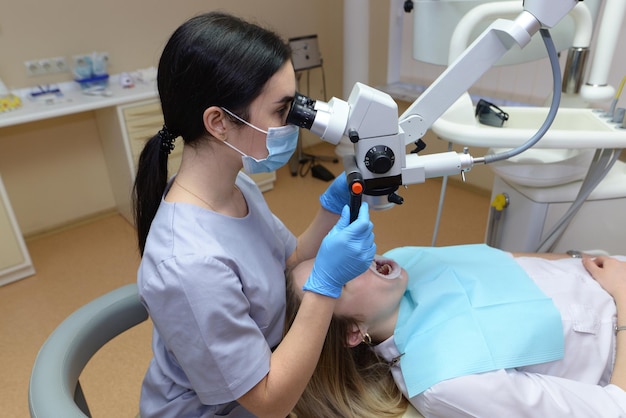 Female dentist examining a young woman looking at her teeth with a professional microscope in a surgical dental office