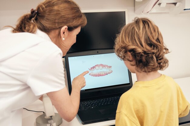 Female dentist explaining 3d teeth scan to faceless boy