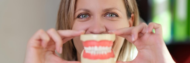 女性歯科医は、彼女の口のデンタルケアと口腔の前に人工の歯を持つプラスチック製の顎を保持しています