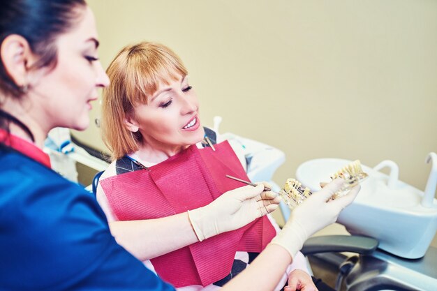 Photo female dentist showing   patient's artificial jaw at the dental office