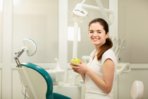 Female dentist smiling and holding a green apple, dental care and prevention concept