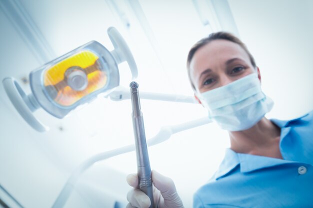 歯科ツールを保持している外科用マスクの女性の歯科医