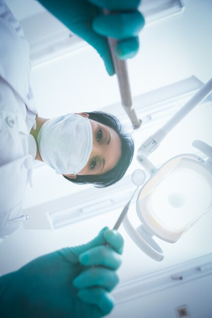 Foto dentista femminile in maschera chirurgica che tiene gli strumenti dentali