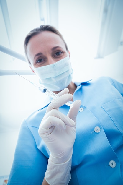 Female dentist in surgical mask holding injection