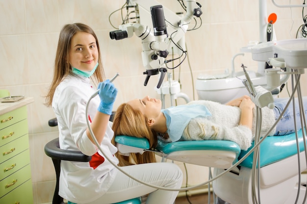 Female dentist treating caries using microscope at the dentist office