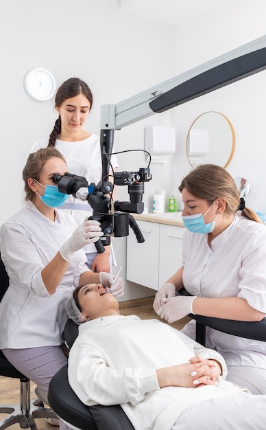 Female dentist using dental microscope treating patient teeth\
at dental clinic office