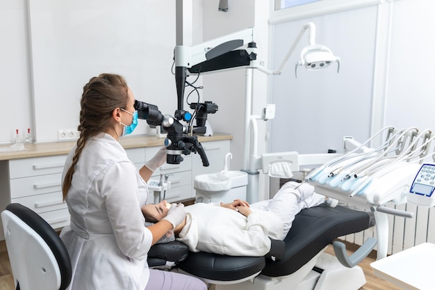 Женщина-стоматолог с помощью стоматологического микроскопа лечит зубы пациента в кабинете стоматологической клиники