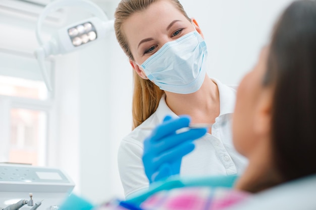 Foto dentista donna che indossa una maschera medica in piedi sotto la lampada di fronte al suo paziente mentre lavora