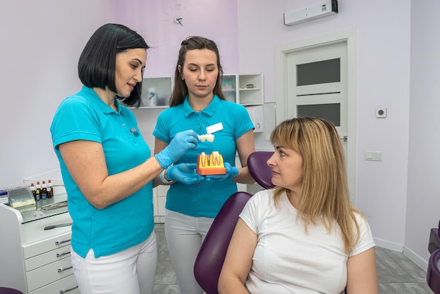 Женщина-стоматолог с ассистентом и пациентом в стоматологической клинике осматривают проблемный зуб