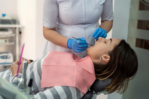 female dentist with dental tools doing procedure of teeth cleaning for her female patient