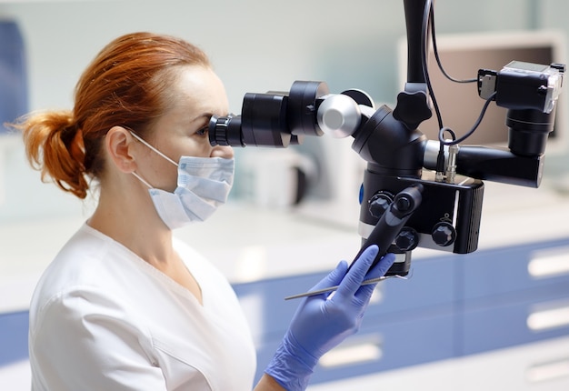 Female dentist with dental tools - microscope, mirror and probe treating patient teeth at dental clinic office, Medicine, dentistry and health care concept, Dental equipment