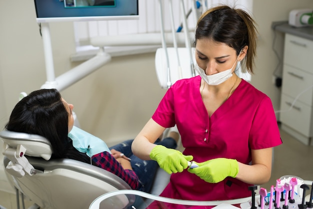 Female dentist at work preparing instruments for examining woman's teeth in dental clinic.