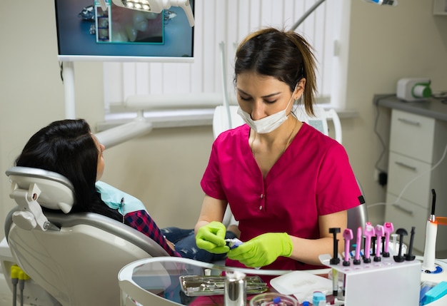 歯科医院で女性の歯を検査するための器具を準備している職場の女性歯科医