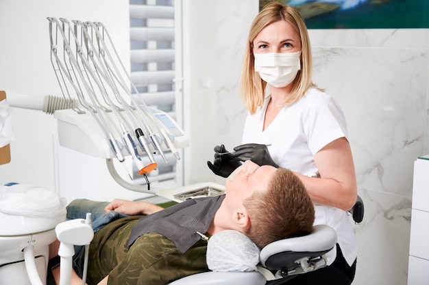 Female dentist at work with patient examining his teeth with dental tools