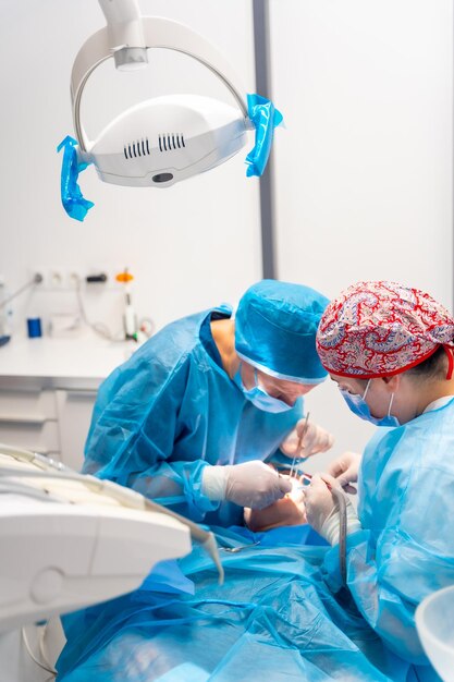 Female dentists in blue scrubs performing a complicated operation on a female patient sucking blood