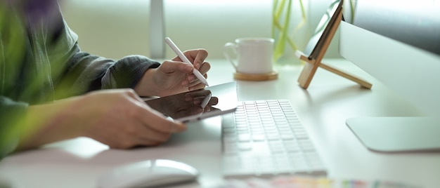 Female designer drawing on digital tablet on office desk with computer device and supplies