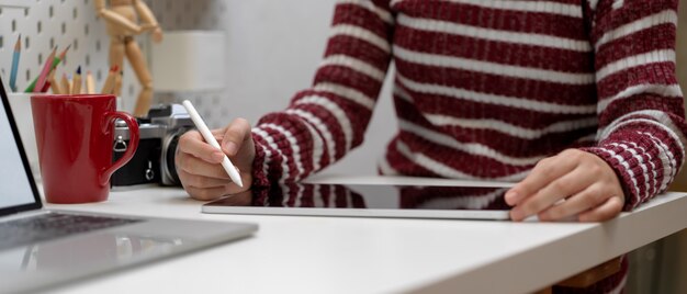 Женский дизайнер работает с цифровым планшетом на белом столе с макет ноутбука, камеры, кружка и принадлежности