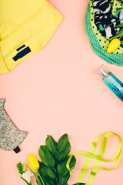 Female desk workspace with cosmetics, light spring clothes, accessories and tulip flowers on yellow background. Spring concept.