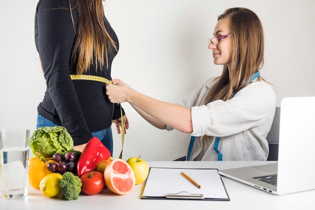 Foto dietista femminile che misura pancia paziente in clinica