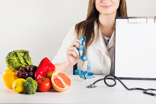 Female dietician's hand holding blank clipboard and measuring tape in clinic