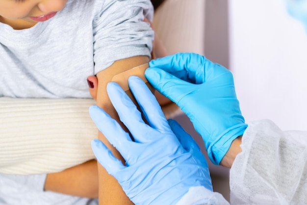 Female doctor applying a plaster to the child after the injection of the vaccine. Vaccination of children. Immunization in the coronavirus pandemic, covid-19