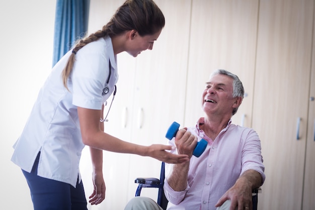 Female doctor assisting senior man in lifting dumbbell