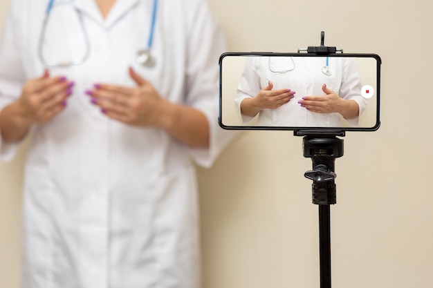 Female doctor blogger recording video on a smartphone standing on a tripod.