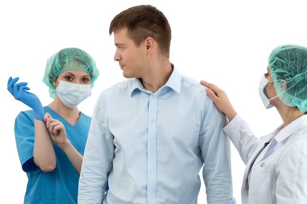 Female doctor in cap and face mask putting on blue protective glove standing behind the scared patient. Her colleague is trying to reassure him. Medical examination. Prostatitis prophylaxis