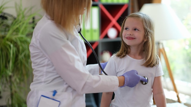 Female doctor checks health of smiling girl in medical clinic therapist listens to heartbeat of