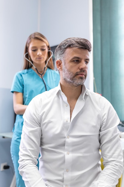 Una dottoressa della clinica esegue l'auscultazione dei polmoni di un paziente con sintomi di coronavirus o polmonite sta tossendo il medico ascolta il respiro sibilante nei polmoni