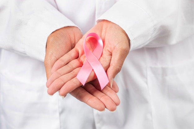 Female doctor closeup on hands holding breast cancer awareness ribbon.