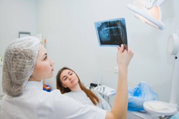 Female doctor dentist examining x-ray of human jaw. Professional stomatologist showing dental x-ray image to patient at clinic office.