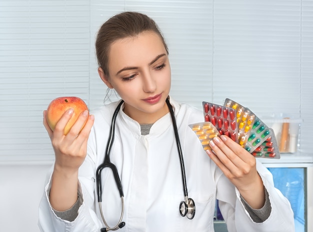 Female doctor or dietologist holds packs of pills and an apple