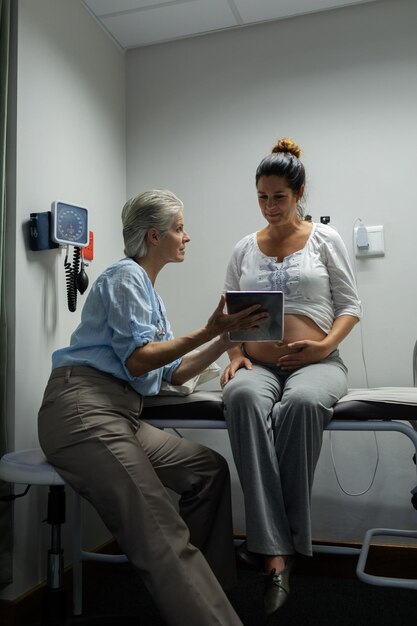 Photo female doctor discussing with pregnant woman over digital tablet in hospital