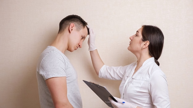 Female doctor examines the male head and fills out the document, taking anamnesis