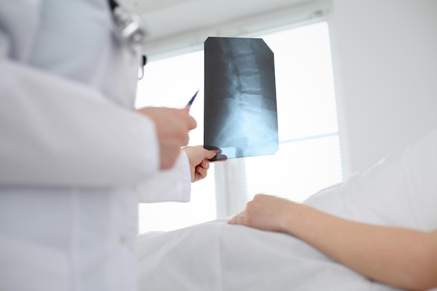여의사는 병원 침대에 누워 있는 환자 옆에 있는 척추의 엑스레이 사진을 검사한다