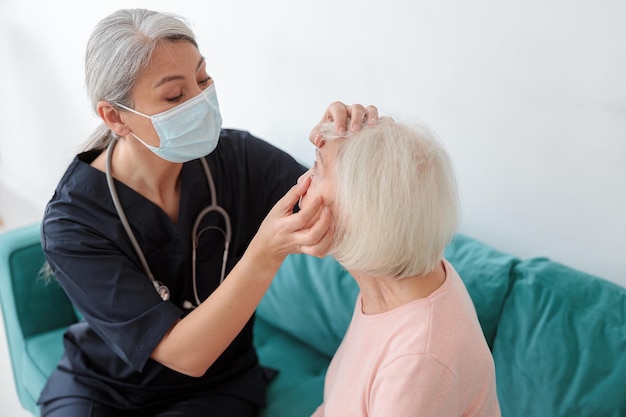 Female doctor examining eyes of elderly woman at home