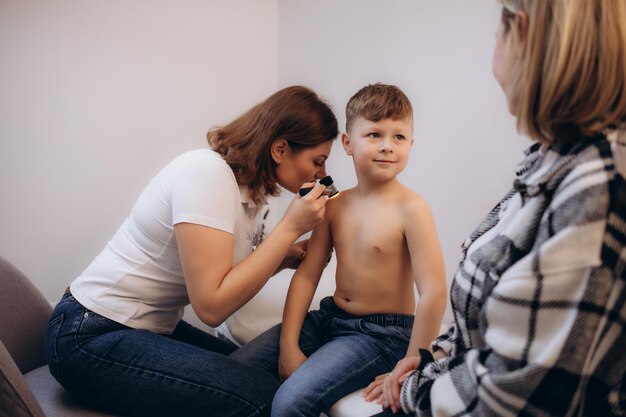 Photo female doctor examining skin of little boy with dermatoscope