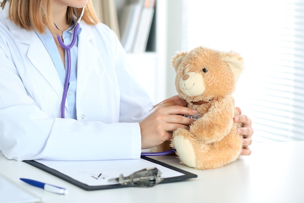 Female doctor examining a   Teddy bear  patient by stethoscope. Children medical care concept